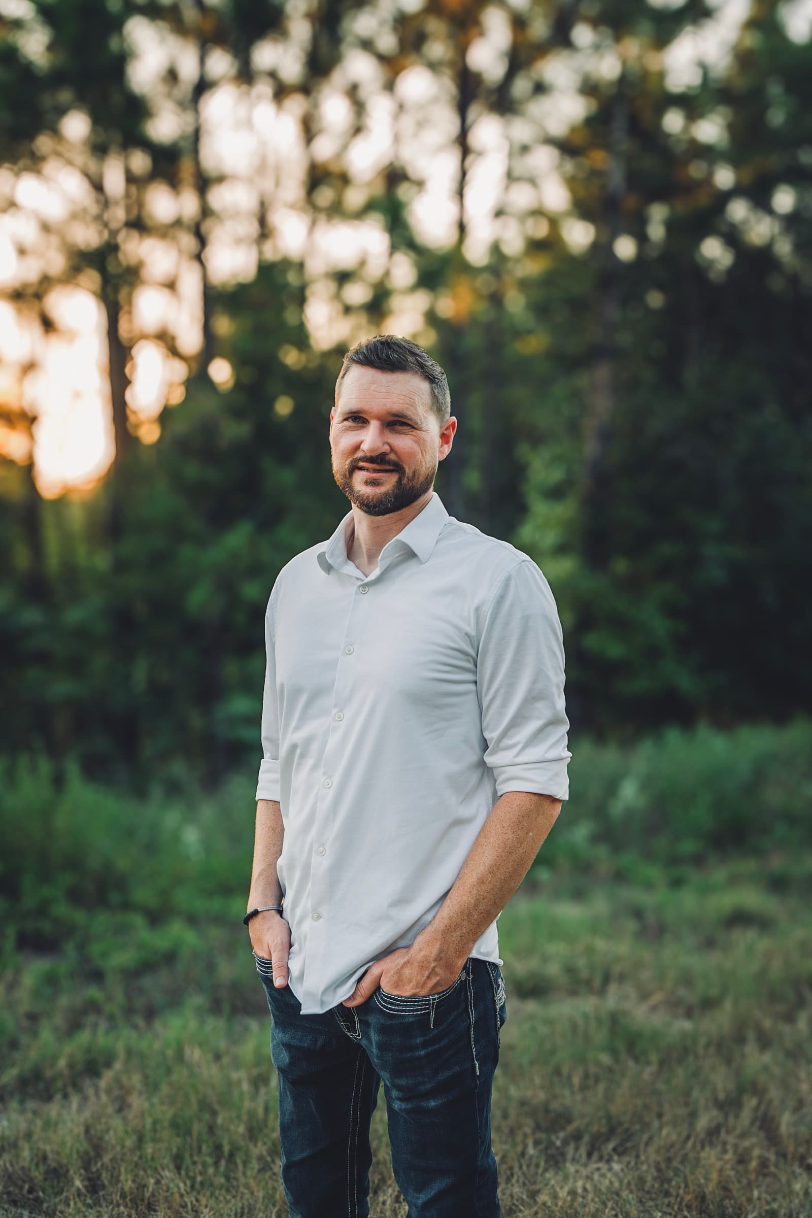 Austin Condiff smiling outdoors at golden hour, wearing a light button-up shirt